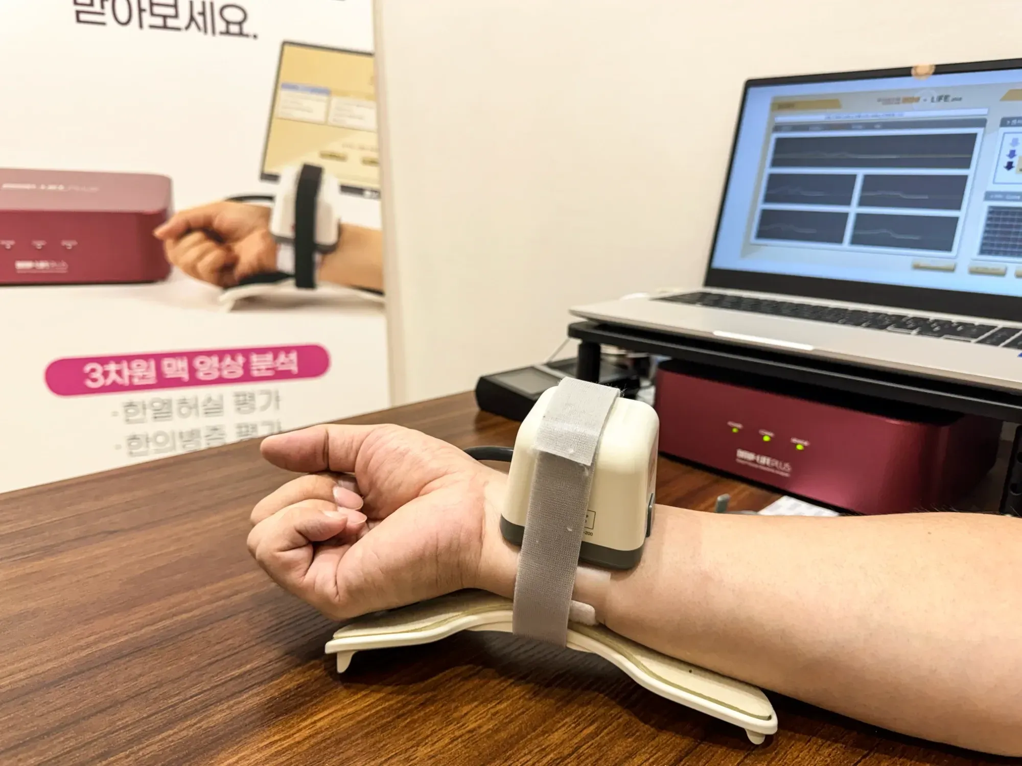 손목에 맥파 측정기를 차고 노트북 화면에 맥파 그래프가 나오는 맥진 검사 장면