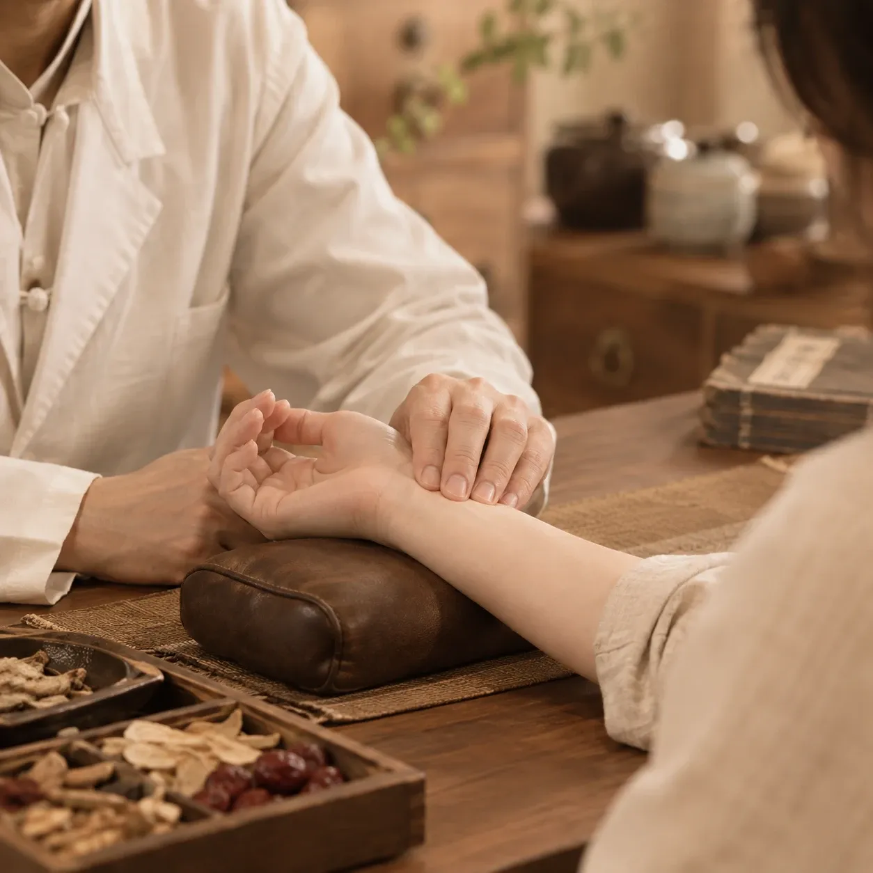 한의사가 환자의 손목에 손가락을 얹어 맥을 짚는 진맥 모습, 앞에 한약재가 놓인 나무 상자가 있음