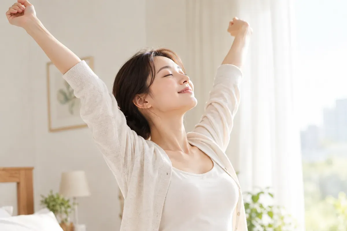 햇살 드는 침실에서 산모가 두 팔을 위로 뻗어 기지개를 켜는 모습